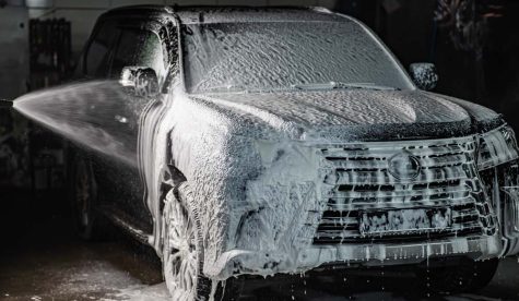 Man applying foam to black car in car wash.